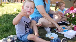 little boy eating a sandwich outside giving a thumbs up