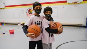 two brothers with basketballs in a gym wearing masks