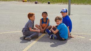 school age boys sitting together on a basketball court smiling