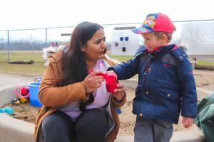 educator and preschool boy paying with sand outside